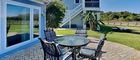 A patio with a round table and four chairs, a covered area with a glass door, and a staircase leading to a balcony.