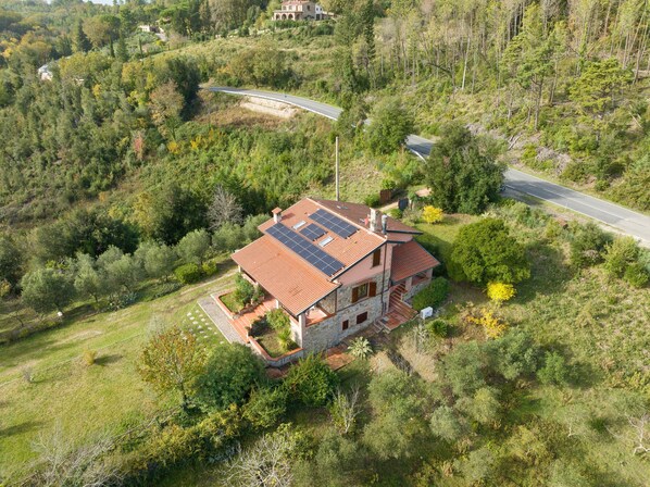 Una casa con techo de tejas rojas, paneles solares y fachada de piedra.