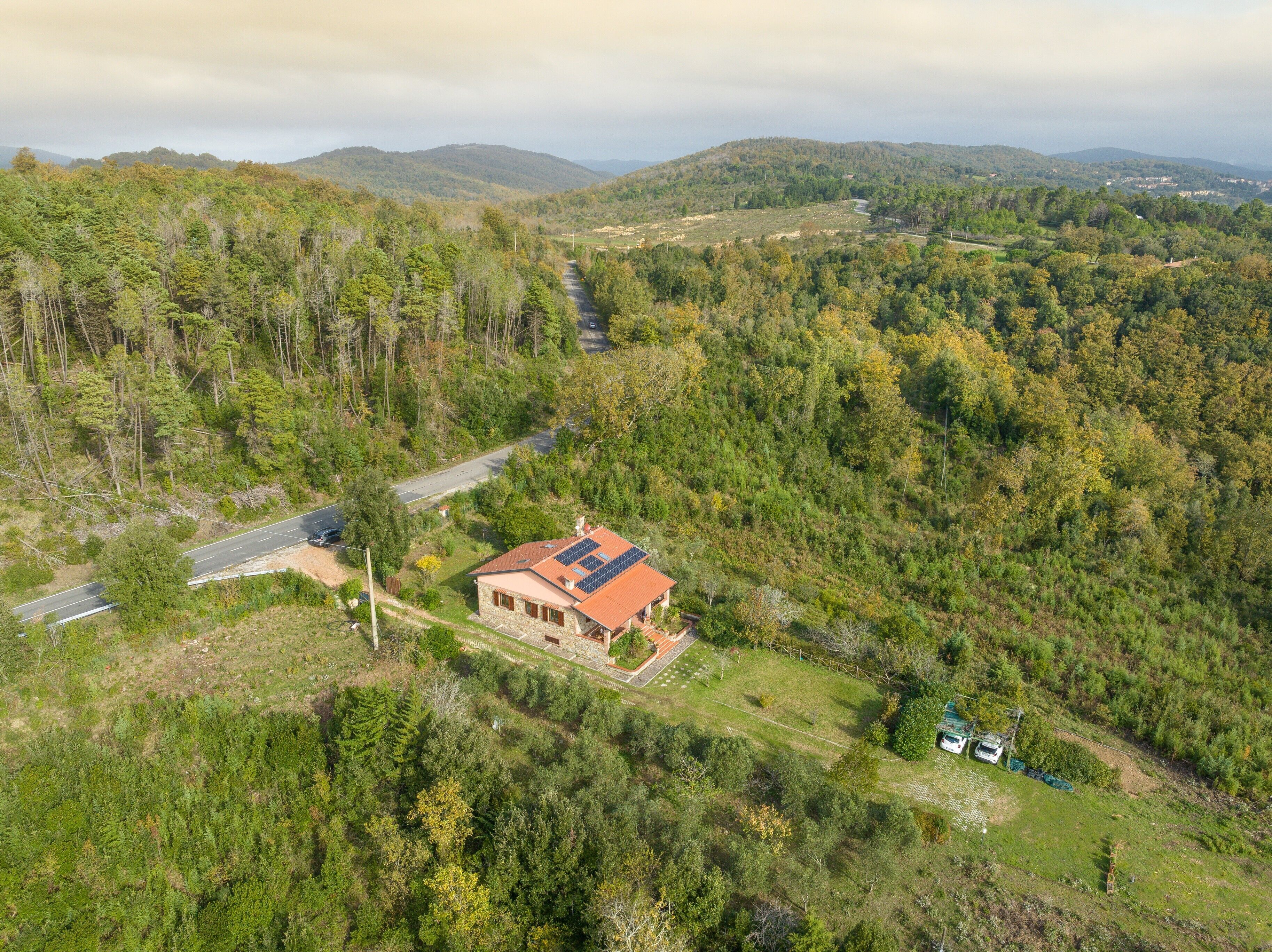 A house with a red roof, surrounded by dense forest and hills.