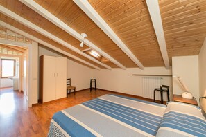 Un dormitorio con techo de madera, una cama con ropa de cama a rayas, una silla, un escritorio con lámpara y un radiador.