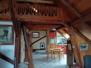 Un interno rustico in legno con zona pranzo, angolo cottura e un balcone con ringhiera decorativa.