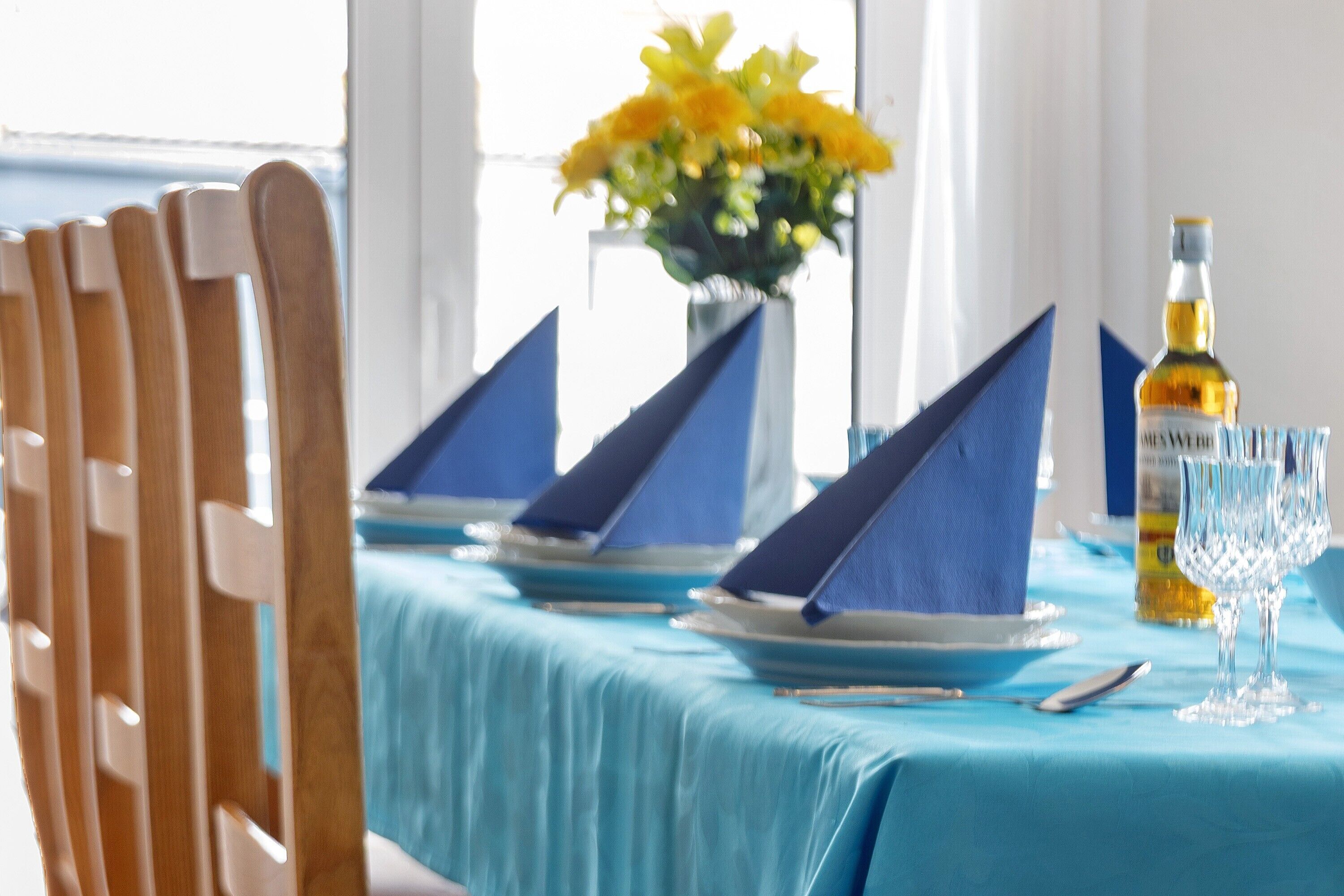 Une table dressée avec des serviettes, des assiettes et une bouteille, et une chaise visible sur la gauche.