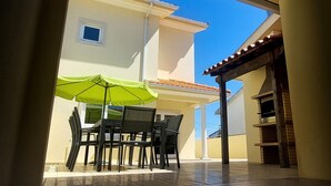 Un patio al aire libre con una mesa, sillas, una sombrilla verde y piso de baldosas.