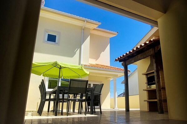 An outdoor patio with a table and chairs, a green umbrella, and a tiled floor.