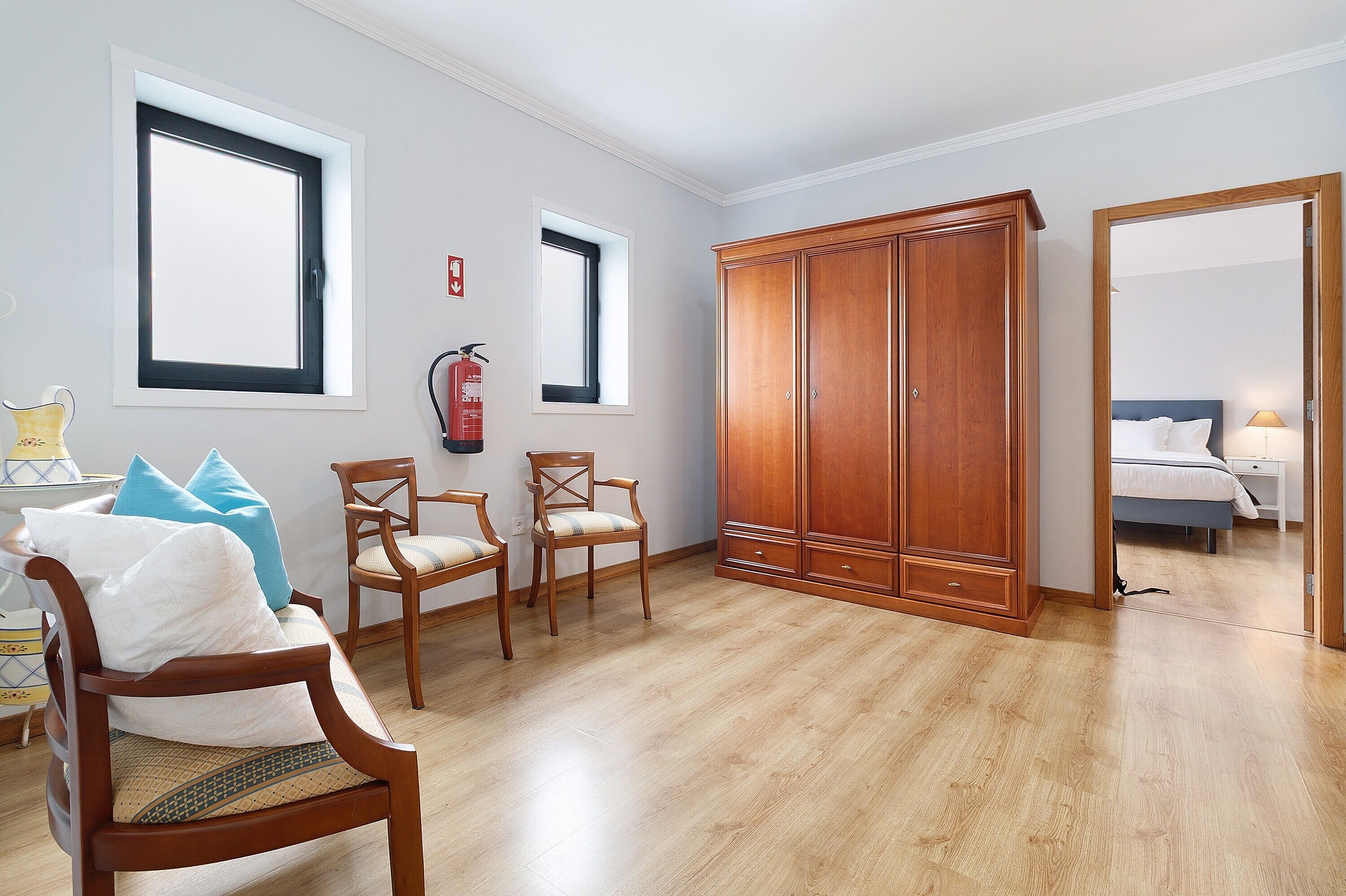 Ein Zimmer mit Kleiderschrank, zwei Stühlen, einem Bett und einem Fenster.