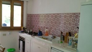 Eine Küche mit weißen Schränken, einem Geschirrspüler, einem Fenster mit Jalousien und einer gemusterten Spritzschutzleiste.