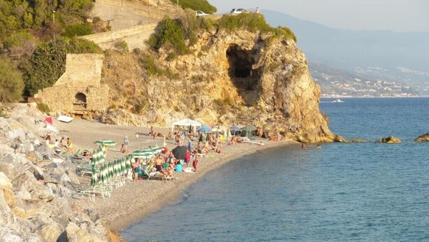 Ein Küstenstrand mit felsigem Gelände, einer herzförmigen Felsformation und freiem Blick auf das Meer.