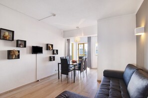 A modern living room with a sofa, dining table, chairs, and wall-mounted TV.