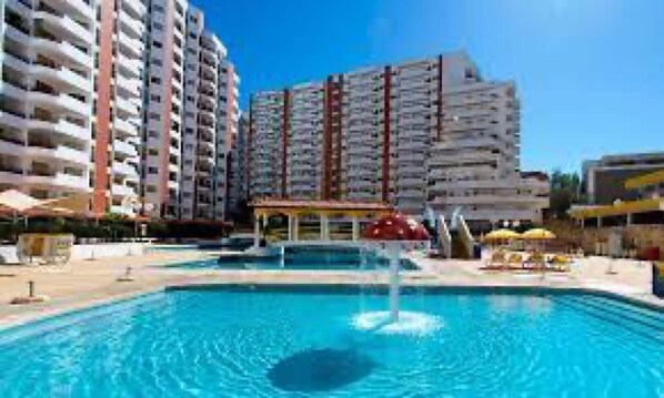 A swimming pool with a fountain, surrounded by high-rise buildings.
