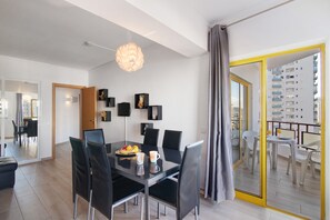 A modern dining area with a glass table, black chairs, and a fruit bowl.