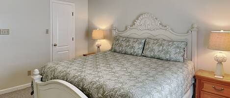 A bedroom with a white bed, floral patterned bedspread, two bedside lamps, a wooden nightstand, and a white door.