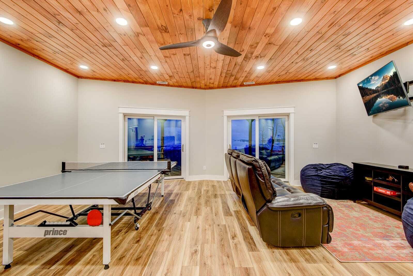 Una habitación con mesa de ping pong, ventilador de techo, sofá, televisor y vistas por las ventanas.