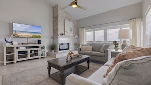 A modern living room with a flat-screen TV, a fireplace, a ceiling fan, and a large window with curtains. - 10 Pipers III – Beachfront Bliss with Ocean Views, Private Balcony & Grill Area (Indian Rocks Beach)