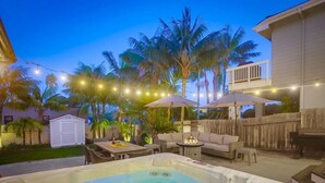 Un jardin avec un jacuzzi, des meubles d’extérieur, des guirlandes lumineuses et des palmiers.