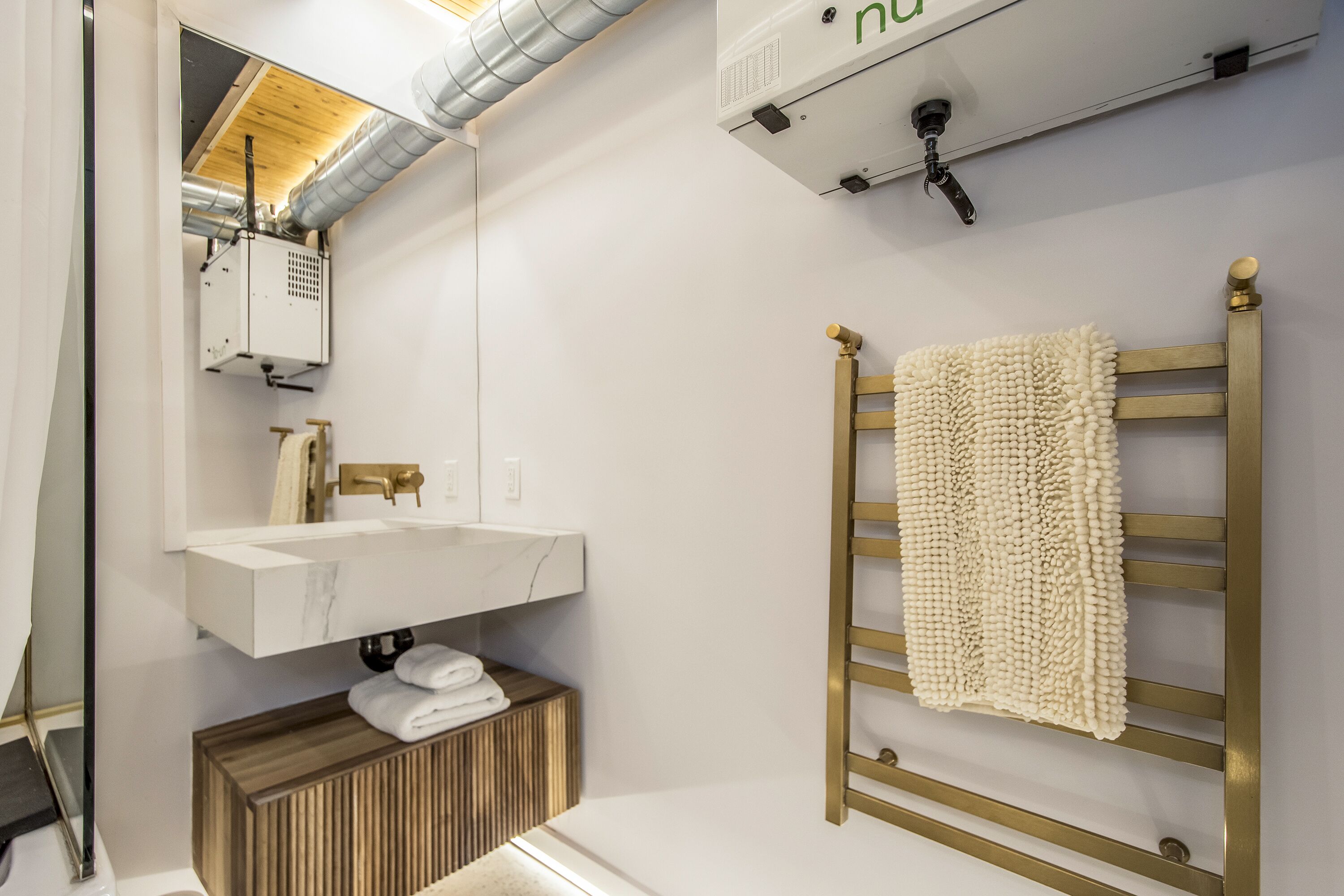 Un baño moderno con lavamanos de mármol, tocador de madera, toallero y aire acondicionado instalado en el techo.