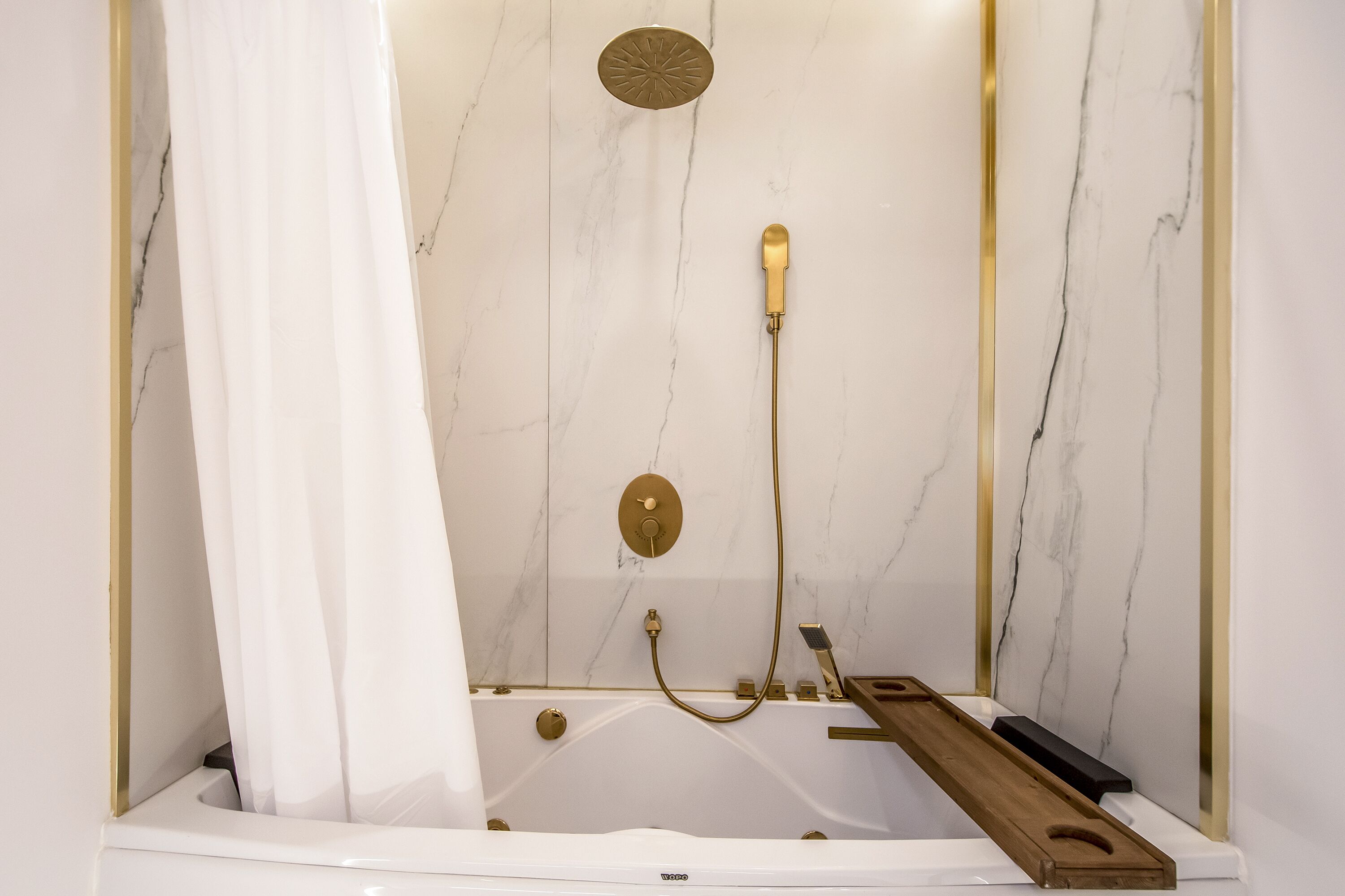 A bathroom with a white bathtub, gold fixtures, and a marble wall.