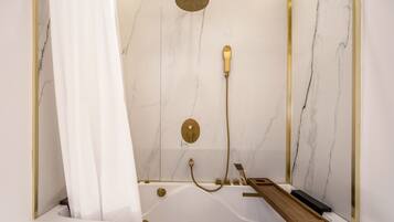 A bathroom with a white bathtub, gold fixtures, and a marble wall.