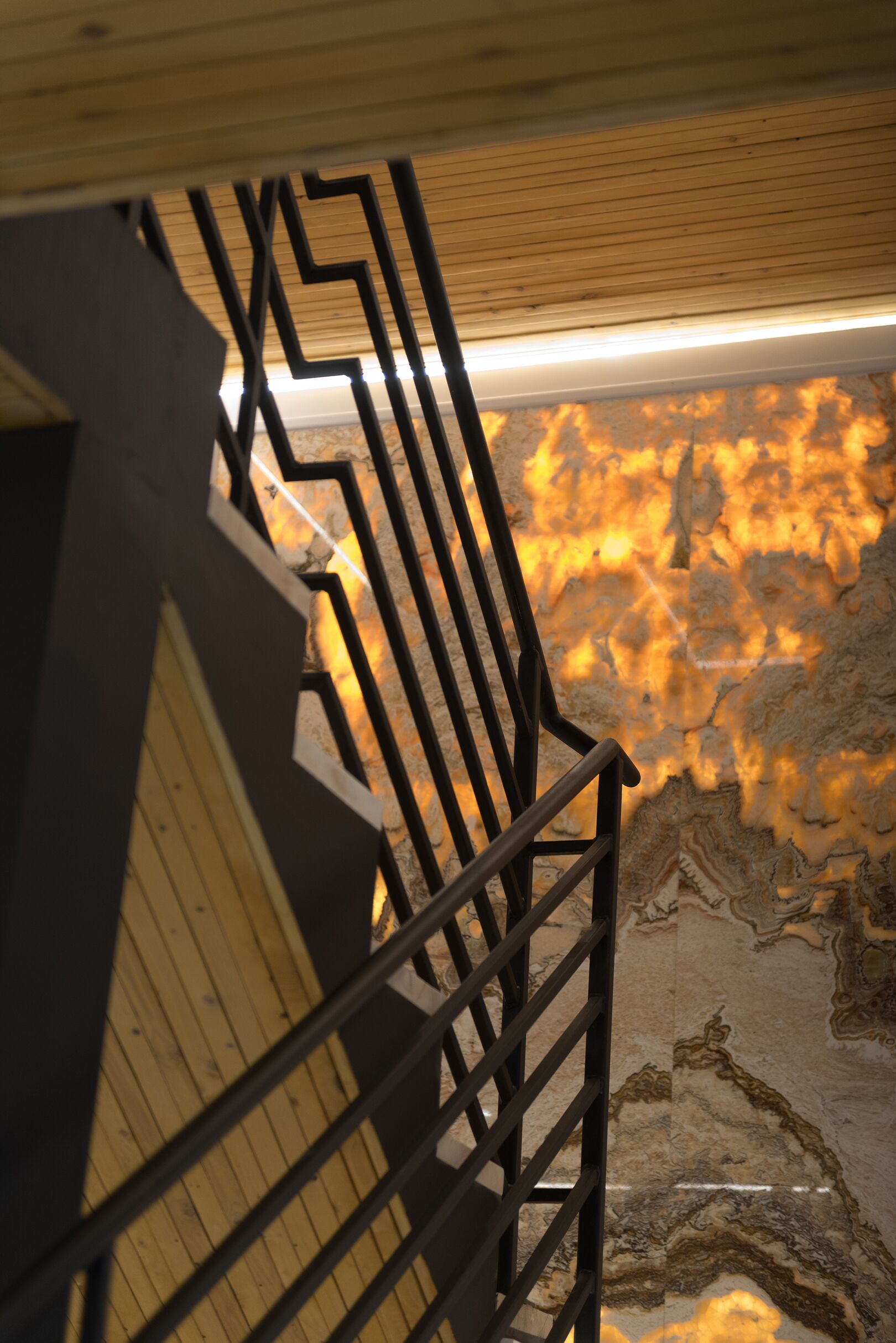 A staircase with a wooden handrail and a metal railing, leading to a room with a marble floor.