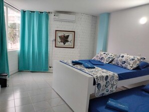Una habitación con cama, ventana con cortinas, aire acondicionado instalado en la pared y un cuadro enmarcado.