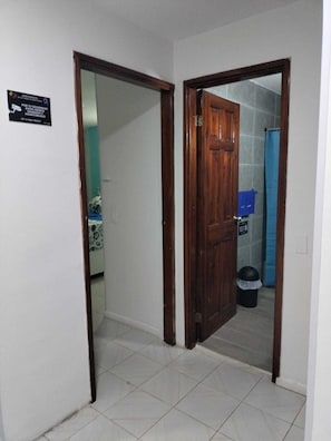 Un pasillo con una puerta de madera que da a un baño. Un cartel en la pared indica vigilancia de seguridad.