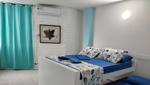 Une chambre à coucher avec un lit, une couvre-lit à motifs bleus et blancs, un tableau encadré au mur et un rideau turquoise.
