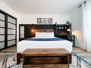 Ein Schlafzimmer mit einem Bett, einem Nachttisch aus Holz, einem Schreibtisch und einem Regalelement.