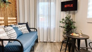 Une pièce chaleureuse avec un canapé bleu, une petite table sur laquelle se trouvent une plante et un verre, et un téléviseur affichant le logo « NETFLIX ».