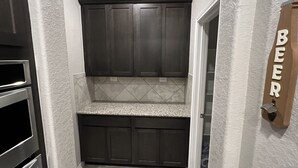 Un couloir étroit avec un coin cuisine intégré, doté de meubles sombres, d’un plan de travail en granit et d’un luminaire encastré au plafond.