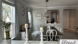 Un coin repas avec une table et des chaises en bois, une plante en pot et un panneau sur lequel on peut lire le mot « béni ».