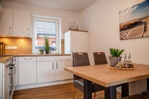 A modern kitchen with white cabinets, a wooden countertop, and a dining area with a wooden table and chairs. - 50068 "deichkajüte 4" - Deichkajüte 4 - Diese Neuwertige Doppelhaushälfte Bietet Ihnen Höchsten (Wittmund)