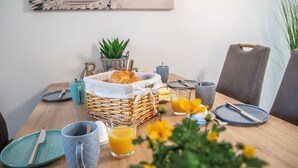 A breakfast table with a wicker basket containing croissants, a glass of orange juice, and a plate with a knife and fork.