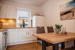 Et moderne køkken med hvide skabe, en træbordplade og et spiseområde med et træbord og stole.