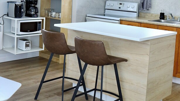 Una cocina moderna con una isla central, dos taburetes para bar, armarios de madera, un microondas, una cafetera y una estufa.