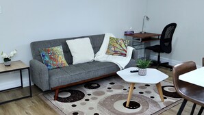 Una sala moderna con un sofá gris, una mesita blanca, una silla de oficina negra y un tapete estampado.
