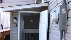 Una entrada residencial con una puerta que da a un garaje, un buzón y un cuadro eléctrico en la pared.