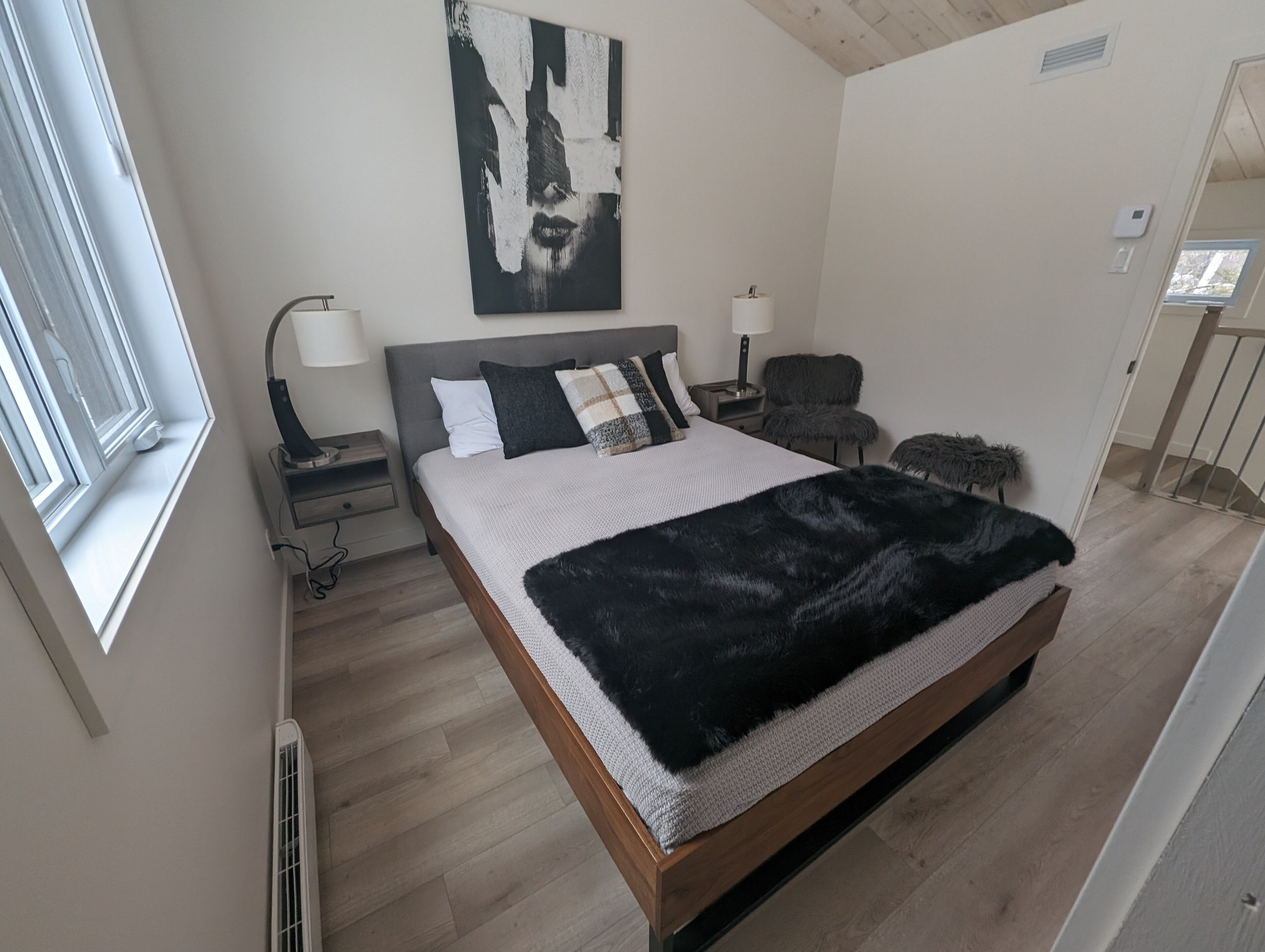 Une chambre à coucher moderne avec un grand lit, une table de chevet, une chaise et un tableau au mur.