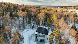 A modern house surrounded by a forest with a snowy ground. - La Châle-heureuse (Baie-Saint-Paul)