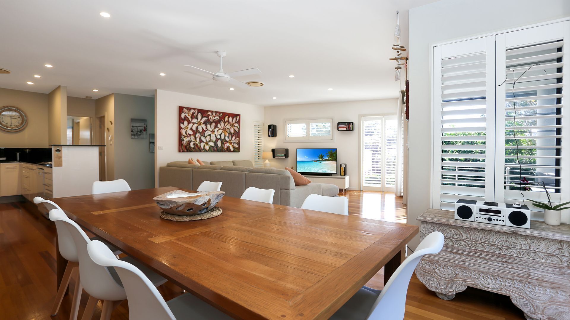 Een moderne woonkamer met een houten eettafel, witte stoelen, een bank en een televisie.
