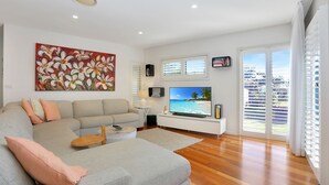 A modern living room with a large flat-screen TV, a beige sofa, a coffee table, and a painting on the wall. - 2 The Pier - Elegance by the Water (Tea Gardens)