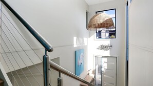 A staircase with a metal handrail, a woven pendant light, a blue door, and a wall-mounted sculpture. - 2 The Pier - Elegance by the Water (Tea Gardens)