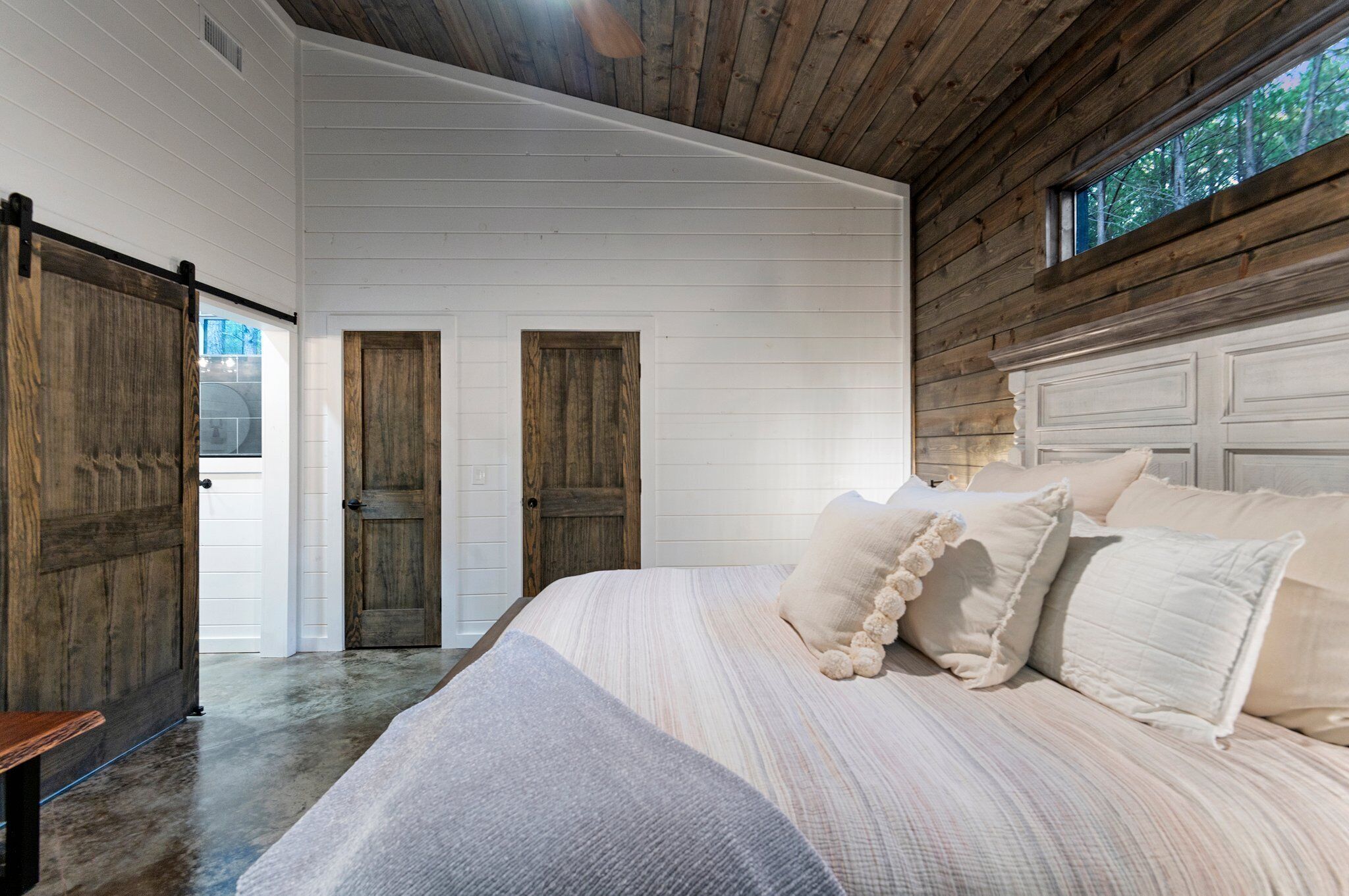 A bedroom with a large bed, wooden walls, and a window.