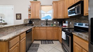 A kitchen with wooden cabinets, granite countertops, a microwave, an oven, and a window with a view. - Cozy Coastal Escape w/ Pool - 1/2 Block to Beach! (South Padre Island)