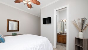 A bedroom with a bed, a television, a mirror, and a door leading to a bathroom. - Cozy Coastal Escape w/ Pool - 1/2 Block to Beach! (South Padre Island)