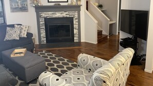 Una sala de estar con chimenea, un sofá, un televisor y una escalera que sube a otro nivel.