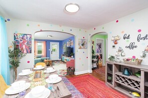 Un salón luminoso y decorado con un comedor, adornos de pared coloridos y una estación de café.