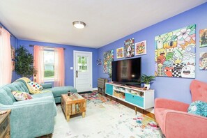 Una sala de estar con un sofá color turquesa, un sillón rosa y un televisor sobre un mueble azul.