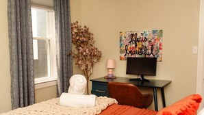 A bedroom with a bed, a desk, a television, and a decorative wall piece.