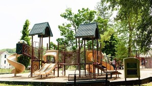 Ein Spielplatz mit Rutschen und Klettergerüsten, umgeben von Bäumen und einer Bank.