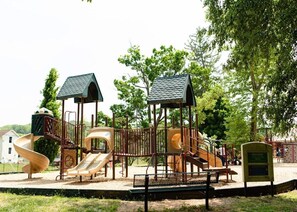 Un parque infantil con toboganes y estructuras para escalar, rodeado de árboles y un banco.