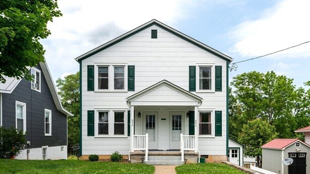 A two-story white house with green shutters, a front porch, and a small attached garage.